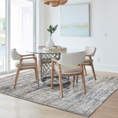 Mesa de jantar com tampo em vidro e quatro cadeiras de madeira e palha branca, sobre tapete cinza azul