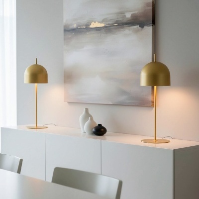 Dois candeeiros de mesa dourados sobre móvel branco com três vasos e pintura abstrata na parede