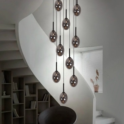 Lustre com várias lâmpadas de vidro fumado em teto dentro de sala branca com escada curva e estante