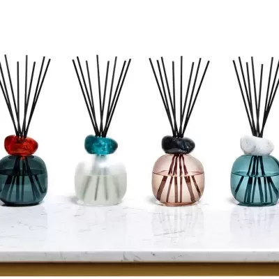 Difusores de fragrância em vidro colorido alinhados sobre mesa de mármore branco