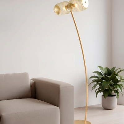 Sofá cinzento claro e candeeiro de pé dourado com abajures de vidro ao lado de planta em vaso cinzento