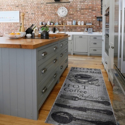 Cozinha com ilha cinza e tampo de madeira, utensílios e tapete cinza com texto em inglês.