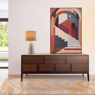 Aparador de madeira com lâmpada de mesa e pintura colorida numa parede branca em ambiente interior claro