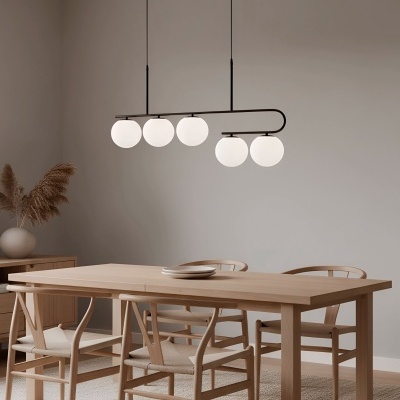 Sala de jantar com mesa de madeira clara, quatro cadeiras, luminária suspensa com globos brancos, vaso com plantas secas