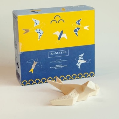 Peça decorativa branca com forma de gaivota e caixa colorida com ilustrações de gaivotas e texto MANULENA
