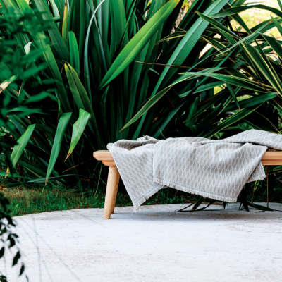 Banco de madeira com tecido cinza ao ar livre e plantas ao fundo