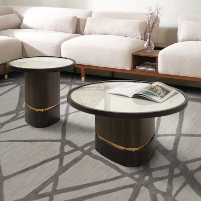 Mesas redondas de centro e auxiliar com tampo em mármore e base em madeira escura, em sala com sofá claro e tapete cinzento com padrões.