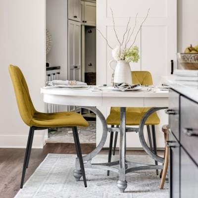 Mesa de jantar redonda branca com duas cadeiras amarelas e vaso branco com flores