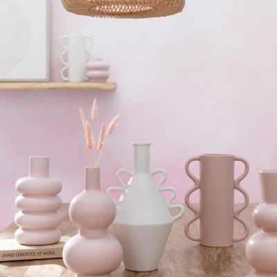 Vasos decorativos em cerâmica rosa e branco sobre mesa de madeira com livro e iluminação rattan