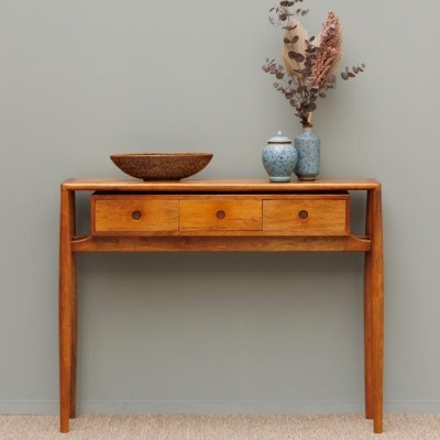 Aparador de madeira com três gavetas, prato rústico e jarros de cerâmica azul clara com flores secas