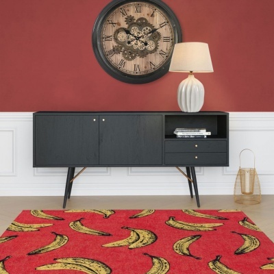 Tapete vermelho com bananas amarelas em frente a aparador preto, lâmpada branca e relógio de parede na sala.