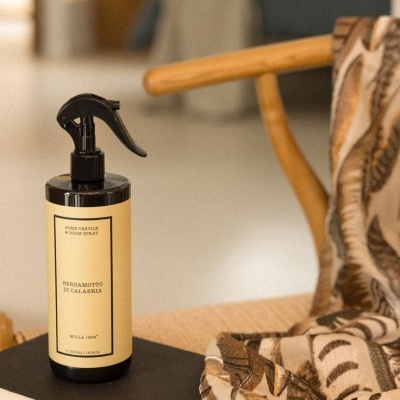 Frasco preto com pulverizador spray de tecidos e corpos em cadeira de madeira com tecido estampado e livro preto