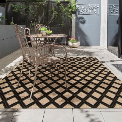Tapete beige e preto com padrão geométrico sob mesa e cadeiras metálicas em área exterior com plantas