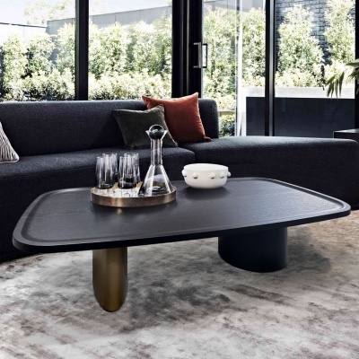 Mesa de centro preta com tampo retangular decorada com garrafa e copos, em sala com sofá cinzento e almofadas coloridas