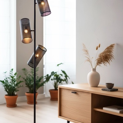 Candeeiro de pé moderno em metal preto com três abajures cilíndricos perfurados e sala decorada com plantas e móvel de madeira.