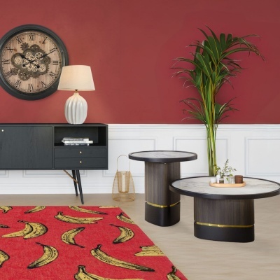 Sala com relógio de parede, móvel preto, candeeiro branco, tapete vermelho com bananas, mesas de centro e planta verde
