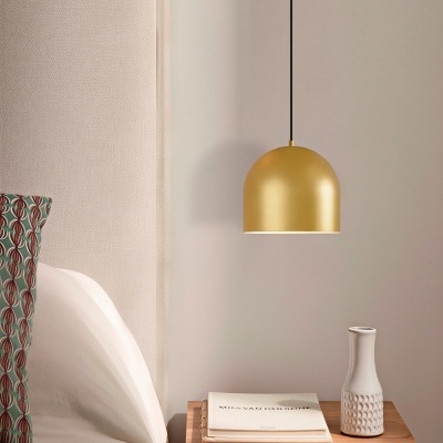 Quarto com cabeceira estofada bege, almofada padrão verde e vermelho, mesa madeira com livro e jarro branco, lâmpada dourada suspensa