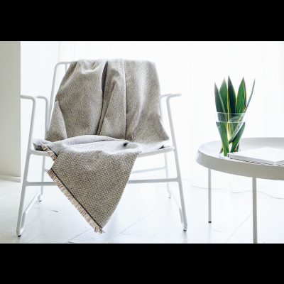 Manta cinzenta numa cadeira branca ao lado de mesa com vaso de planta