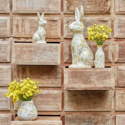 Estatuetas de coelho e vasos de cerâmica branca com flores amarelas em nichos de madeira rústica.