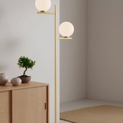 Candeeiro de pé dourado com duas esferas brancas ao lado de móvel de madeira clara e planta em vaso