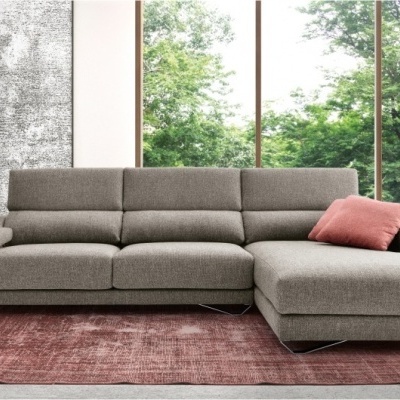 Sofá chaise longue cinzento com almofada rosa numa sala moderna com janelas grandes e planta decorativa
