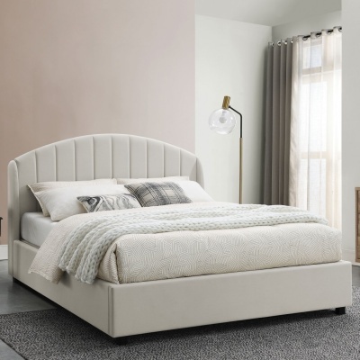 Cama de casal creme estofada com cabeceira curva, roupa de cama com padrão geométrico, manta branca trançada, almofadas decorativas, candeeiro de pé dourado e cortinas claras