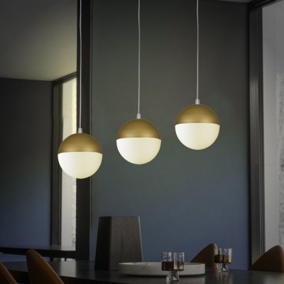 Três candeeiros redondos suspensos dourados e brancos em sala moderna
