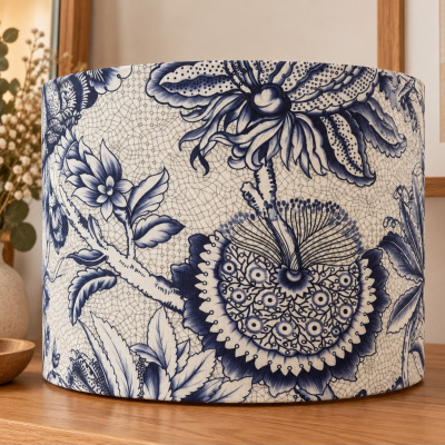 Abajur com padrão floral azul e branco em mesa de madeira, com flores secas ao fundo.