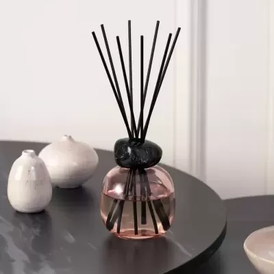 Difusor de fragrância com base em vidro cor de rosa e pedras pretas no topo em mesa preta