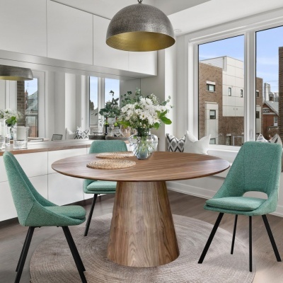 Mesa redonda de madeira escura com cadeiras verdes num ambiente luminoso
