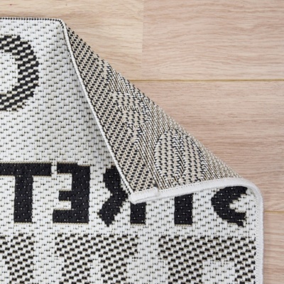 Tapete branco e preto com padrão geométrico e pontos sobre chão de madeira