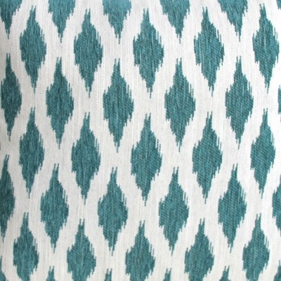 Almofada com padrão geométrico azul-esverdeado em fundo branco.