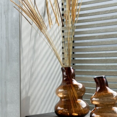 Vaso decorativo em vidro castanho com plantas secas sobre superfície preta