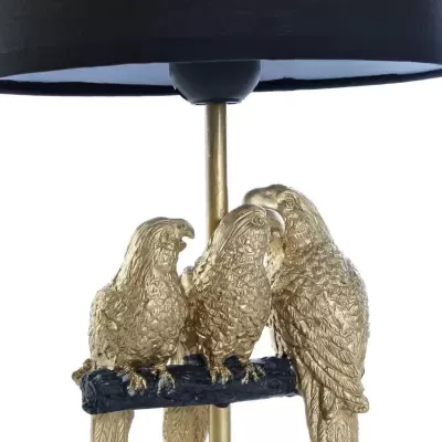 Candeeiro com base dourada com três papagaios e abajur preto cilíndrico.