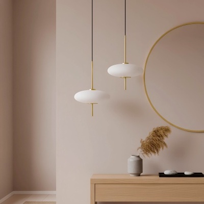 Candeeiros pendentes brancos com detalhes dourados sobre mesa de madeira clara com vaso e espelho redondo dourado.