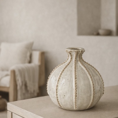 Vaso decorativo de cerâmica bege com textura e linhas verticais salientes sobre mesa de madeira clara