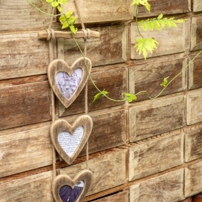 Quadro decorativo de madeira com corações pendurado numa parede de madeira e plantas verdes