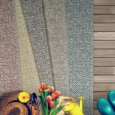 Quatro tapetes geométricos coloridos alinhados sobre chão de madeira com ferramentas de jardinagem e flores.