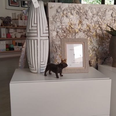 Mesa de cabeceira branca com lâmpada cinzenta, moldura de foto bege e figura de cão preto