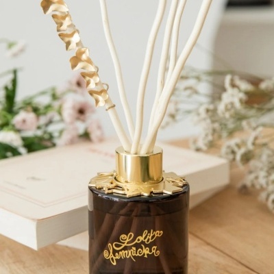 Frasco difusor de ambiente em vidro escuro com hastes brancas e detalhes dourados