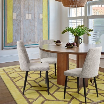 Mesa de jantar redonda em madeira com quatro cadeiras estofadas e vaso com plantas numa sala luminosa