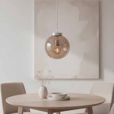 Sala de jantar com mesa redonda de madeira clara, quatro cadeiras bege, vaso com flores secas, pratos brancos e candeeiro suspenso de vidro fumado marrom.