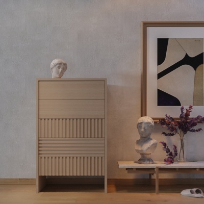 Móvel em madeira clara com gavetas e detalhes em ripado, bustos esculturais brancos e vaso de flores roxas junto a quadro abstrato