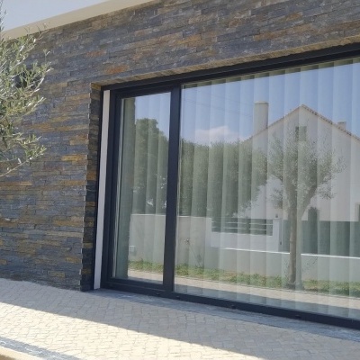 Porta de vidro de correr com moldura preta numa parede de pedra cinza exterior