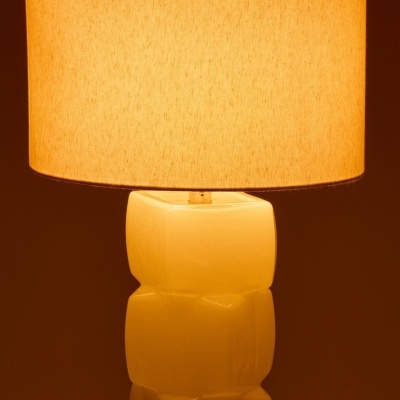 Candeeiro de mesa com base branca cerâmica e abajur bege iluminado