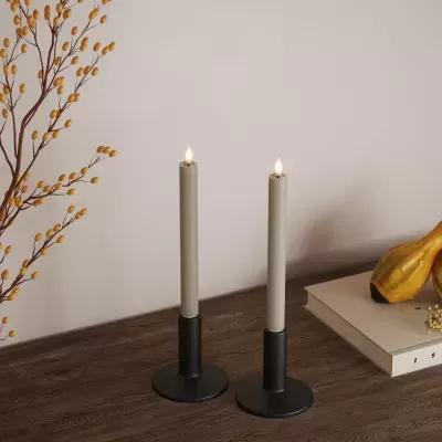 Dois castiçais pretos com velas brancas acesas sobre mesa de madeira com decoração e livros