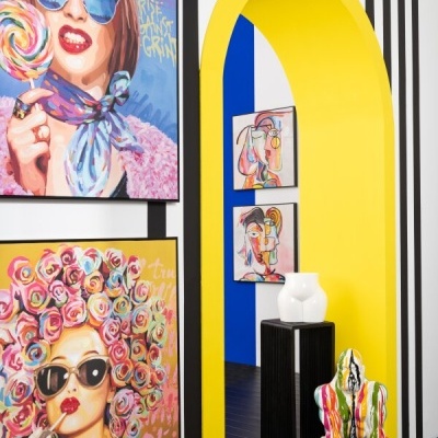 Parede riscada preta e branca com quadros coloridos e arco amarelo com escultura de cão colorido no chão