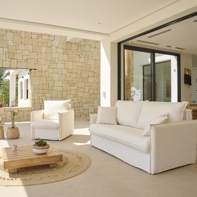 Sofá e poltrona brancos em tecido com mesa de centro em madeira e tapete redondo de fibras naturais, parede de pedra clara
