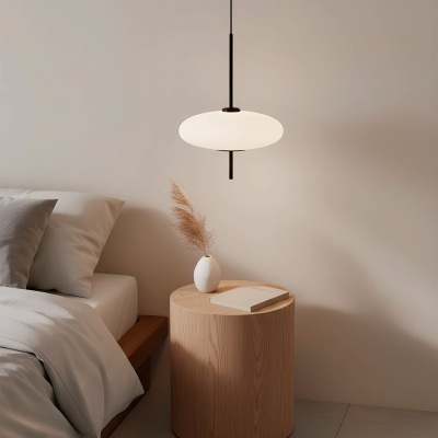 Mesa de cabeceira redonda em madeira clara com vaso branco e livro, ao lado de cama com roupa de cama cinza claro