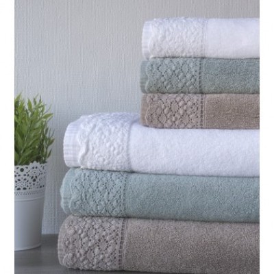 Toalhas empilhadas em branco, verde-água e bege com bordado ao lado de planta em vaso branco.